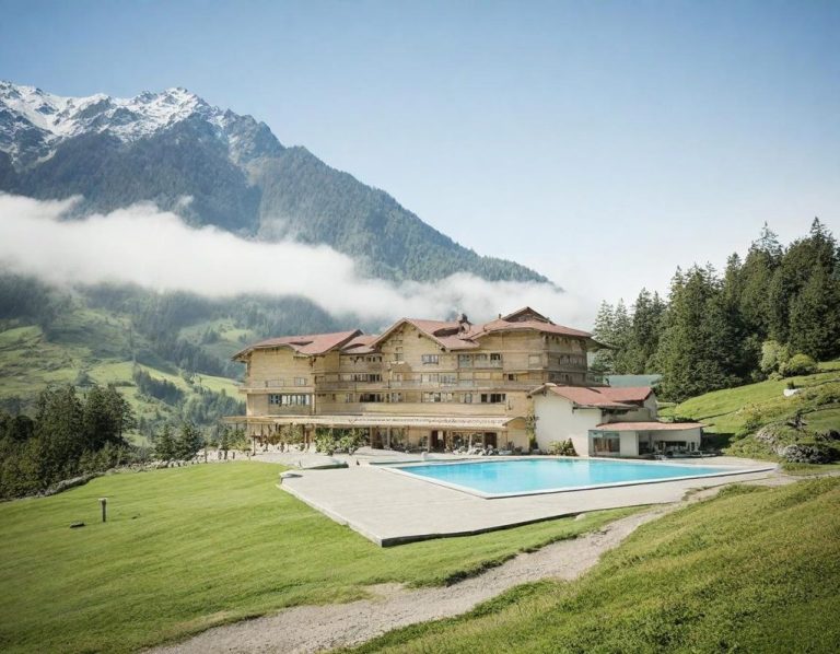 Berglandschaft mit einem Hotel und einem Pool, umgeben von grünen Wiesen und Bergen.